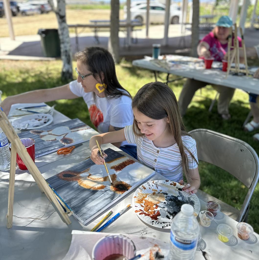 Two girls work on their paintings at an outdoor painting class.